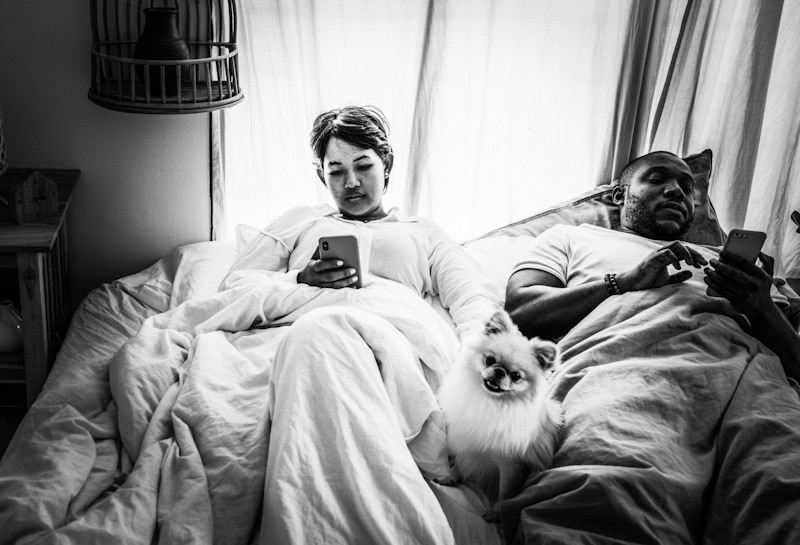 Photo showing a couple on bed distracted by their phones